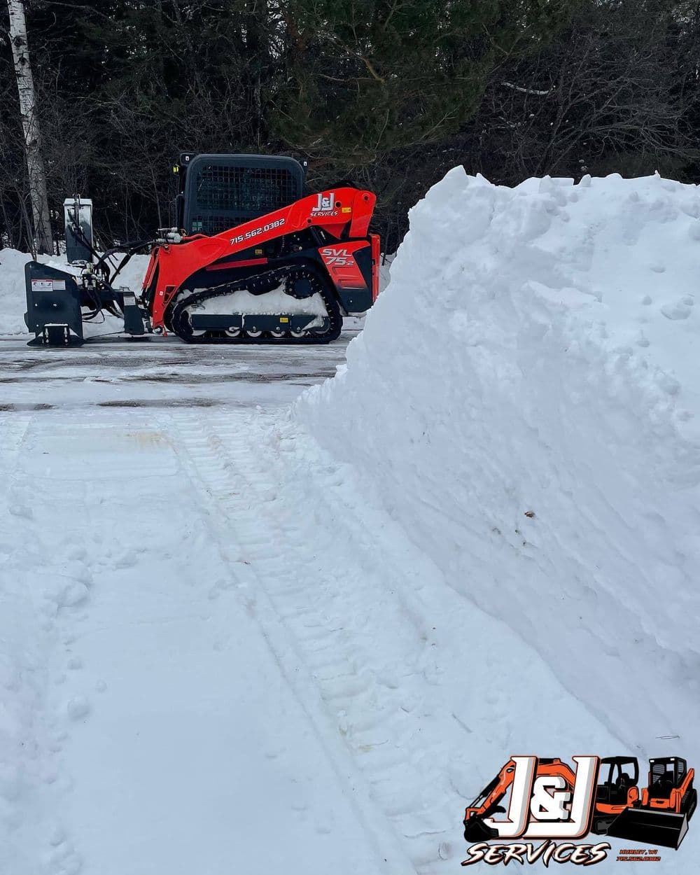 Bobcat snow removal equipment next to a tall snow bank, featuring J&L Services branding.
