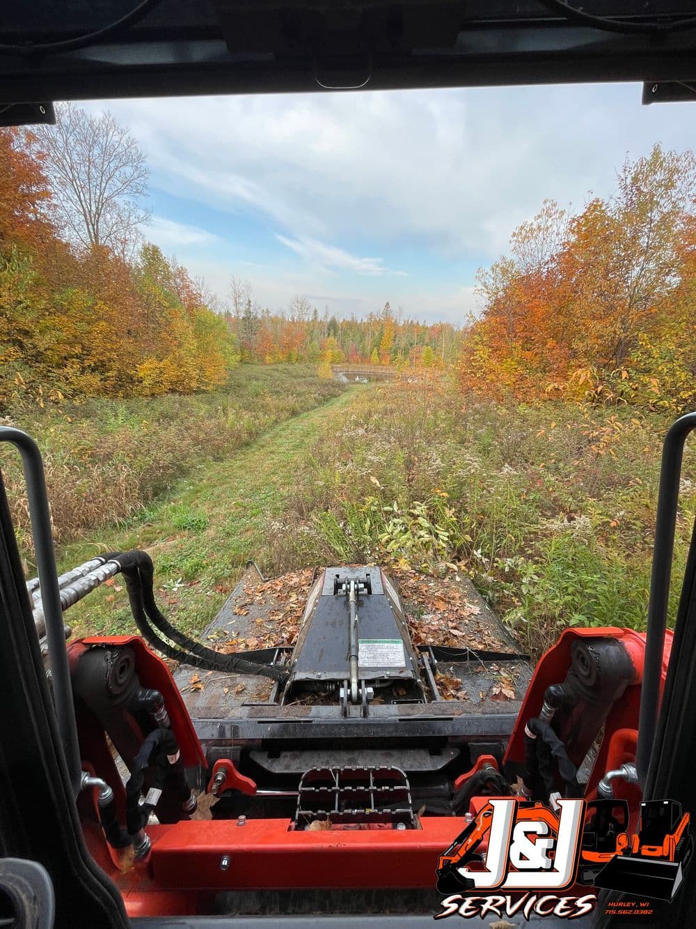 View from a tractor cabin overlooking a fall landscape trail with colorful foliage.